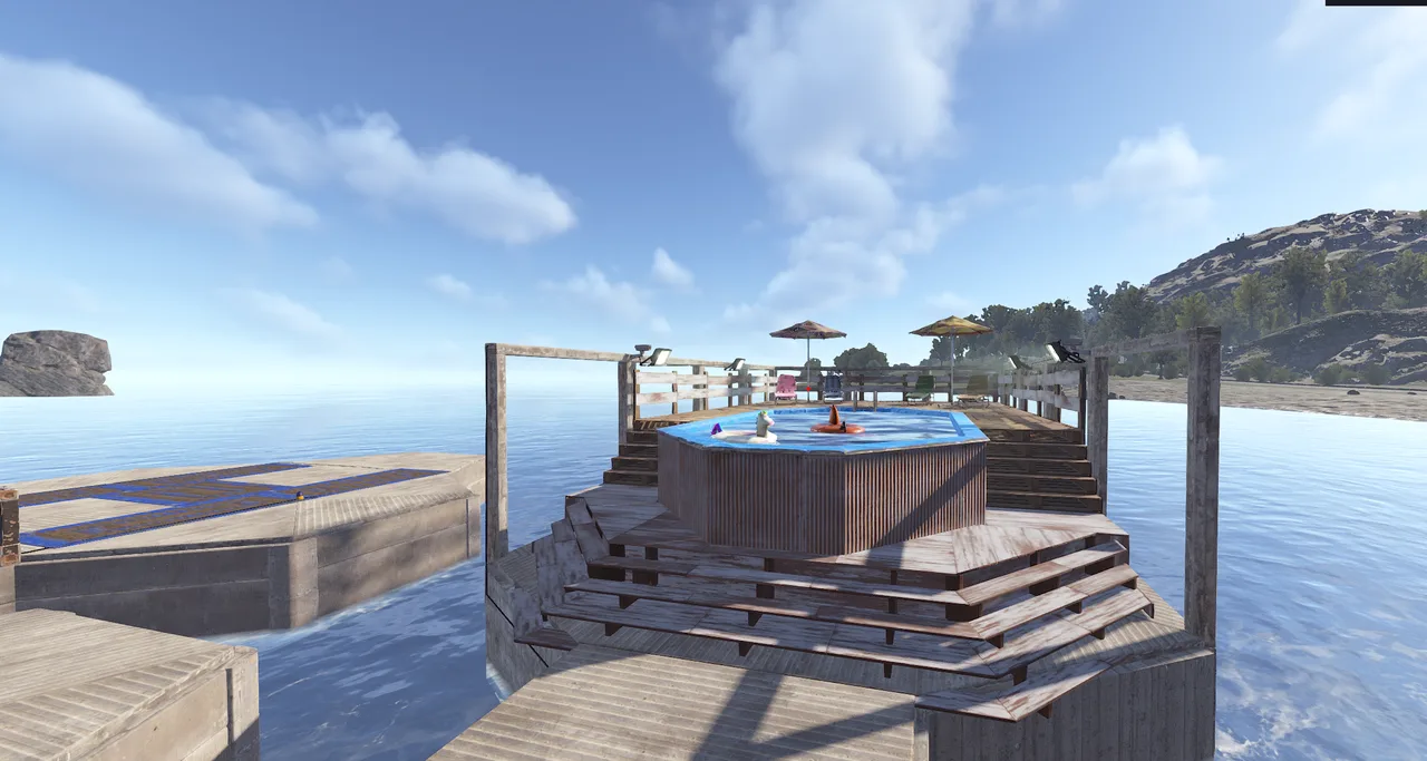 Rust town built on wooden platforms over water, featuring a pool, umbrellas, mountains, and sea